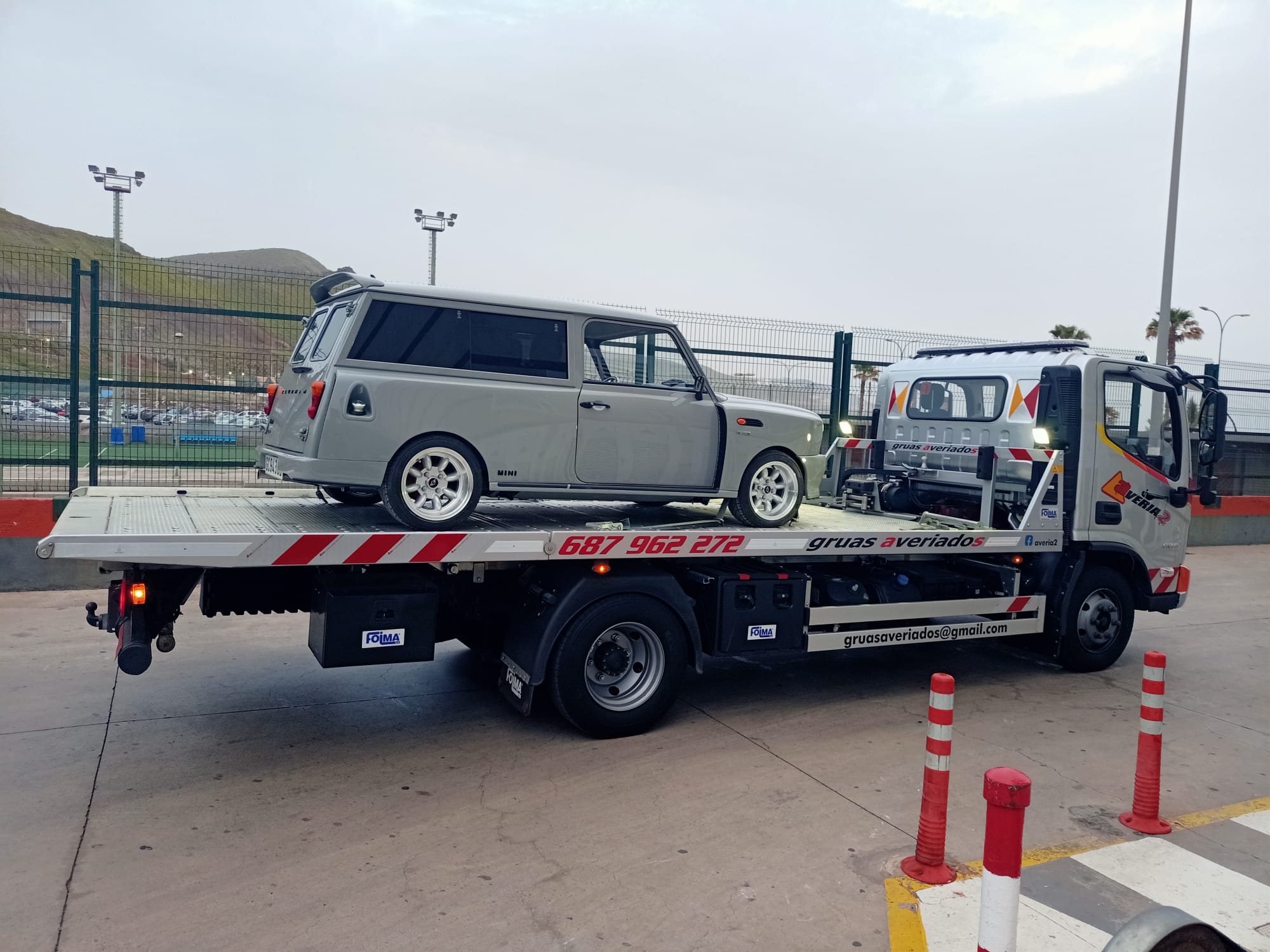 Grúa transportando un Mini clásico gris de colección