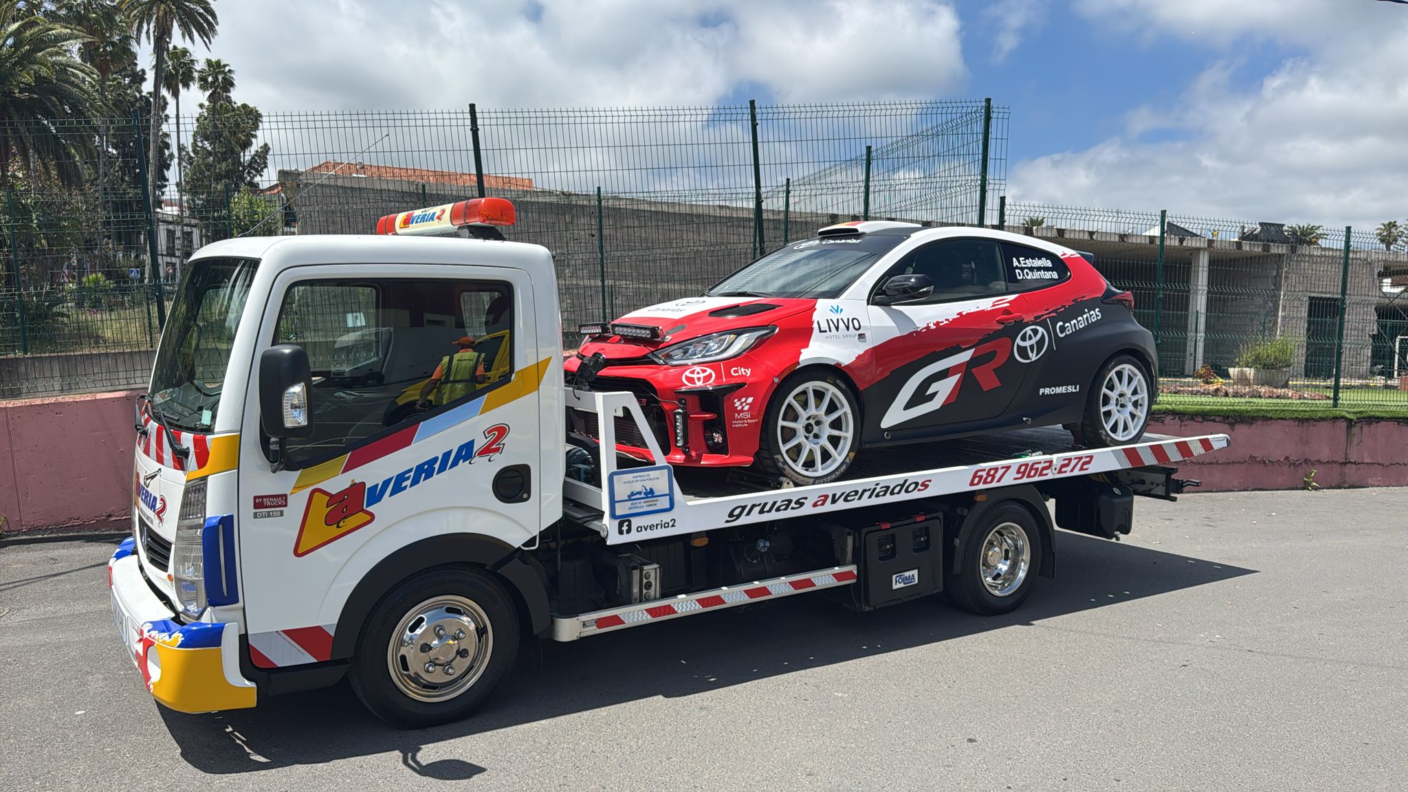 Grúa de Averiados transportando un coche de rally Toyota GR con palmeras de fondo