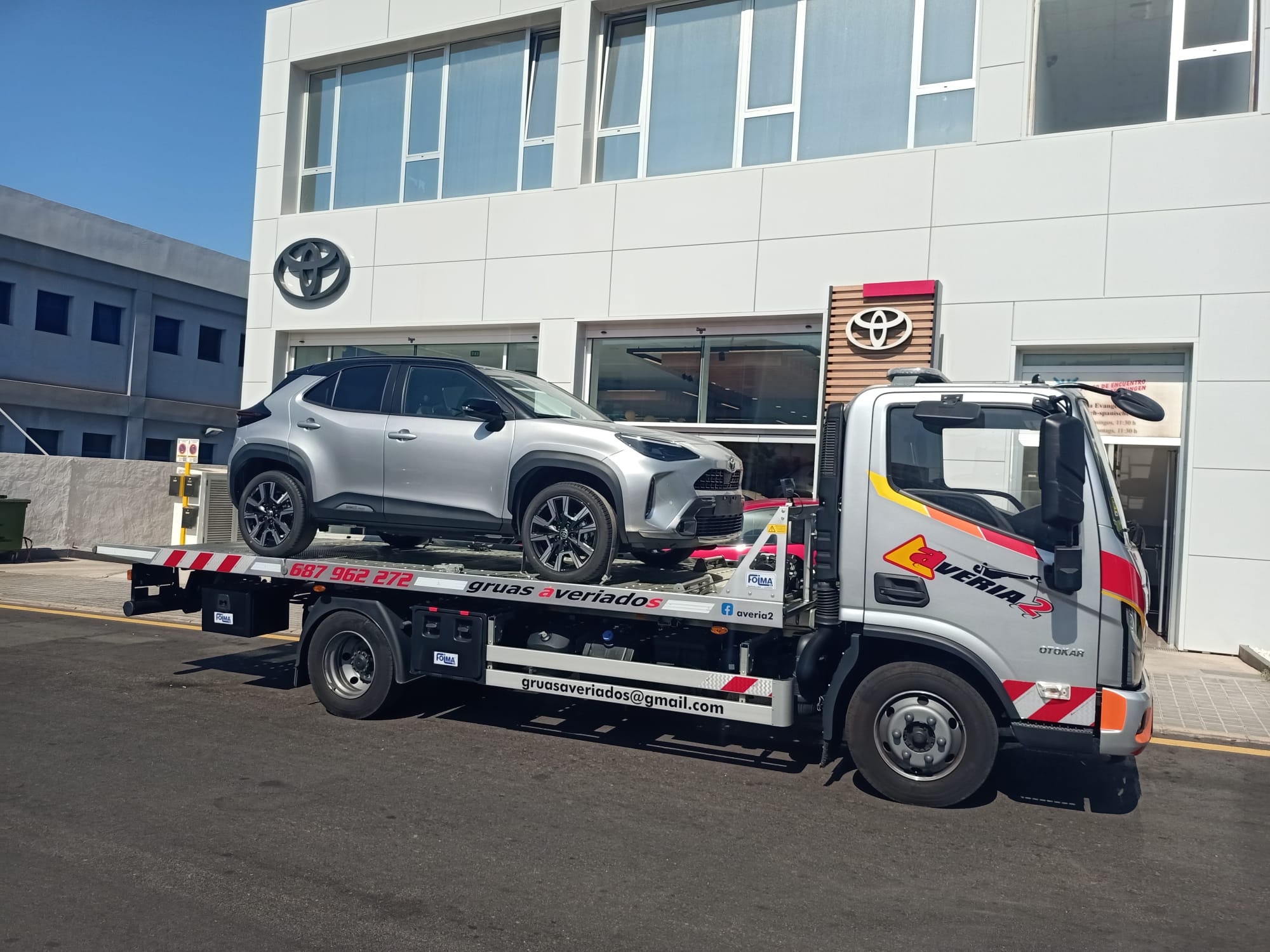 Grúa plataforma de Averiados cargando un SUV Toyota nuevo frente a un concesionario